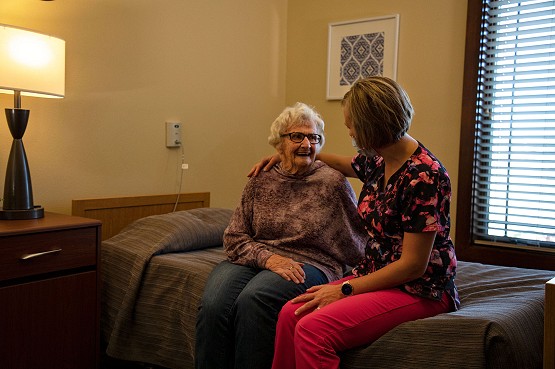 Pine Haven resident sitting on bed and talking with a Certified Nursing Assistant