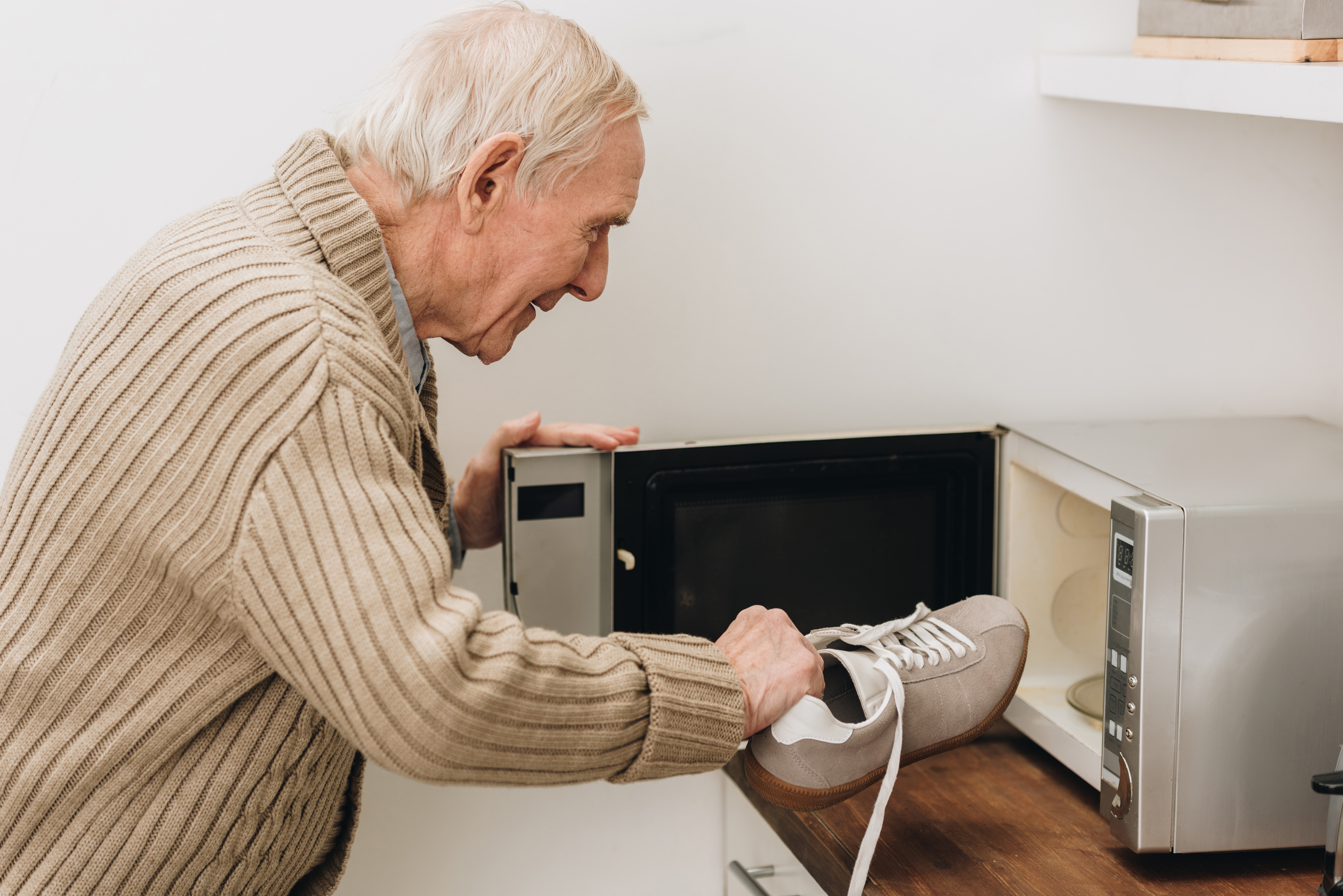 retired man with dementia disease putting shoe in microwave oven